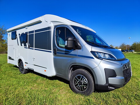 Moderner Campervan auf grünem Feld bei sonnigem Himmel.