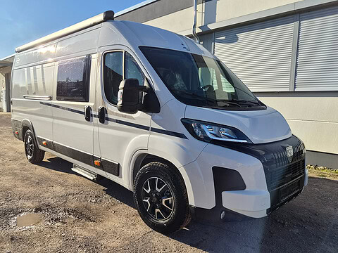 Weißer Fiat Ducato Camper mit schwarzen Felgen und großen Fenstern.