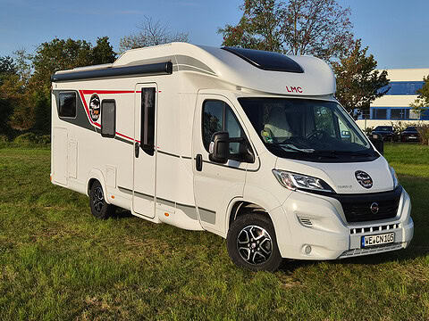 Weißes LMC Wohnmobil auf grünem Rasen mit Bäumen im Hintergrund.